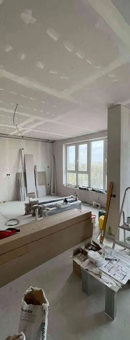 Open-plan apartment renovation in progress with drywall ceiling, materials on site, and large windows, Rimmart project