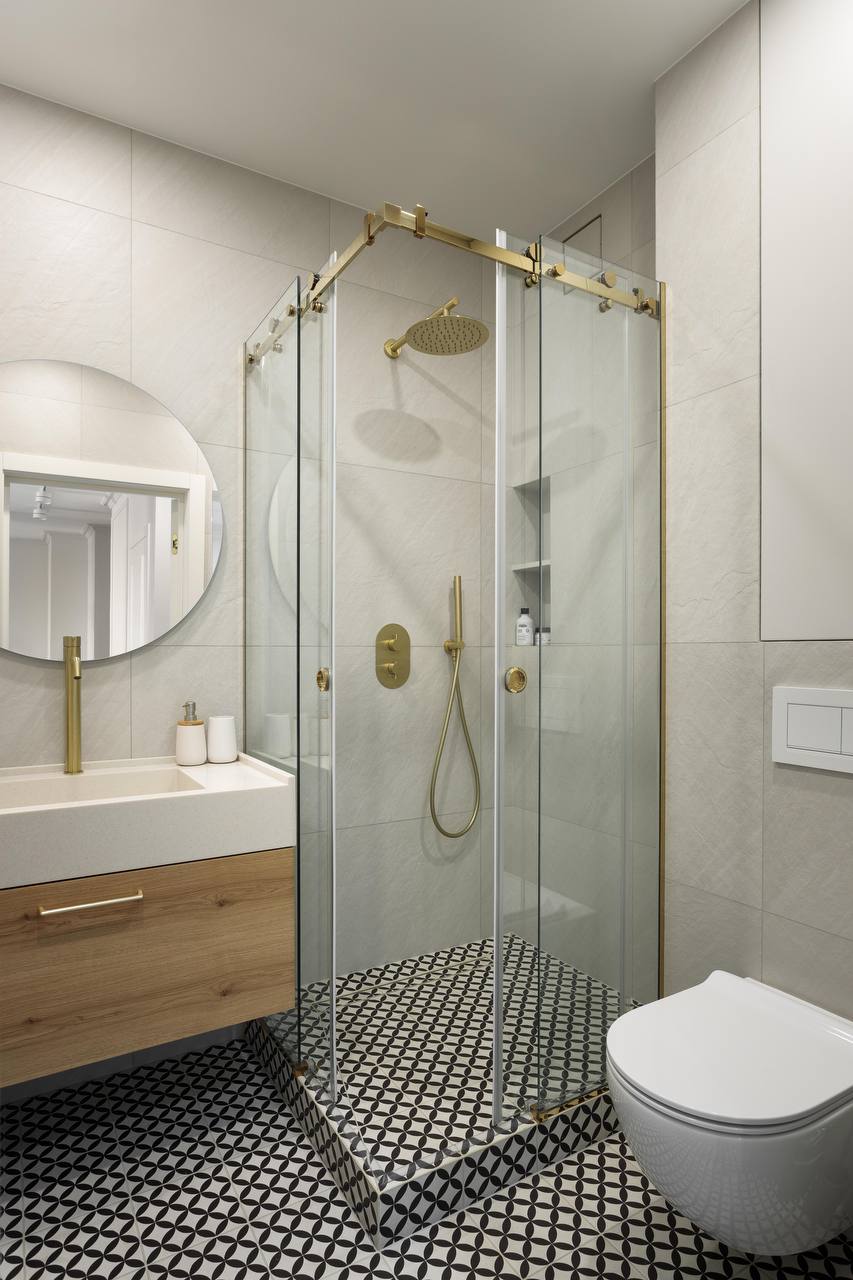 Bathroom with glass shower enclosure, brass fixtures, vanity with wood finish, and patterned floor tiles