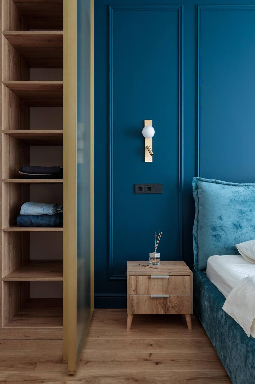 Bedroom accent wall in deep blue with mouldings, bedside table, and brass wall sconce