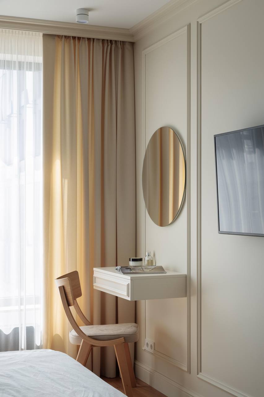 Bedroom corner with wall molding, floating vanity desk, round mirror, and beige curtains.